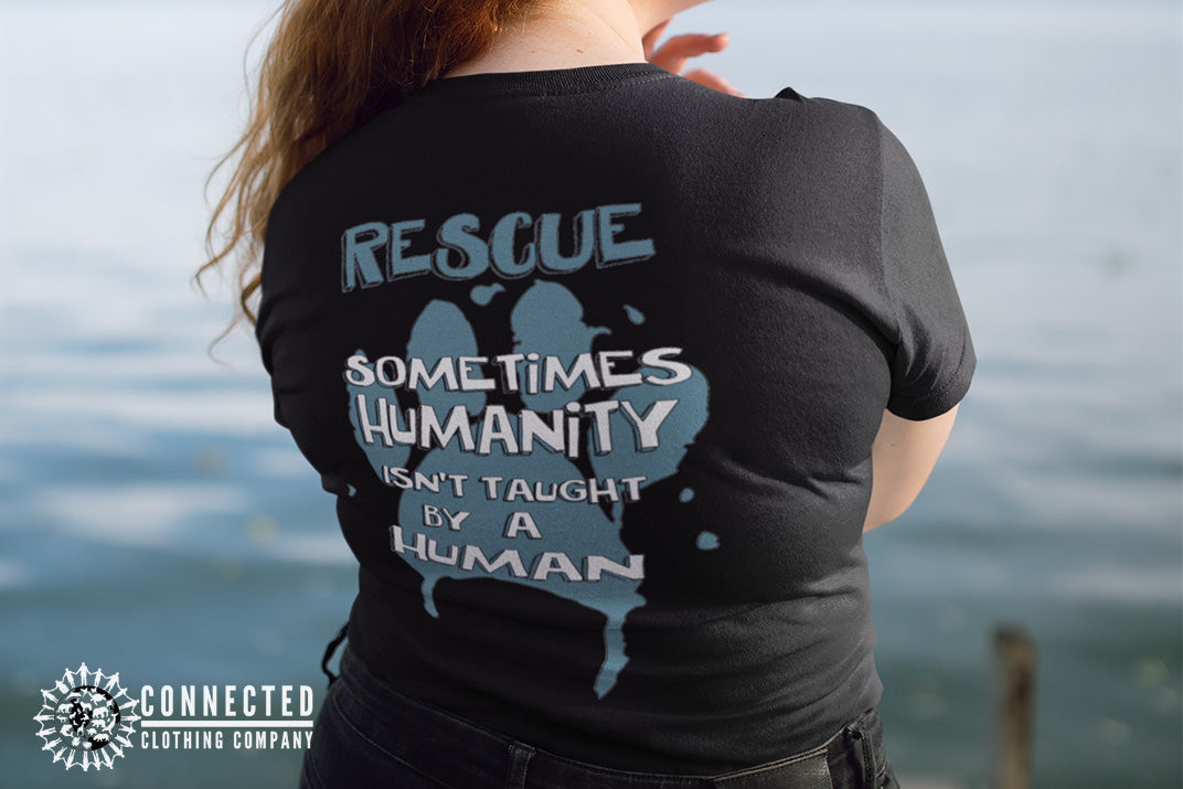 Model wearing Black Show Humanity Tee at the lake that reads "Rescue. Sometimes humanity isn't taught by a human" - marktwainstoryteller - Ethically and Sustainably Made - 10% donated to the Society for the Prevention of Cruelty to Animals